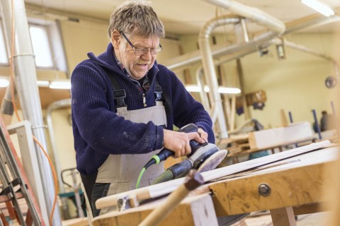 Ein Mann arbeitet mit einem Schwingschleifer an einem Holzbalken.