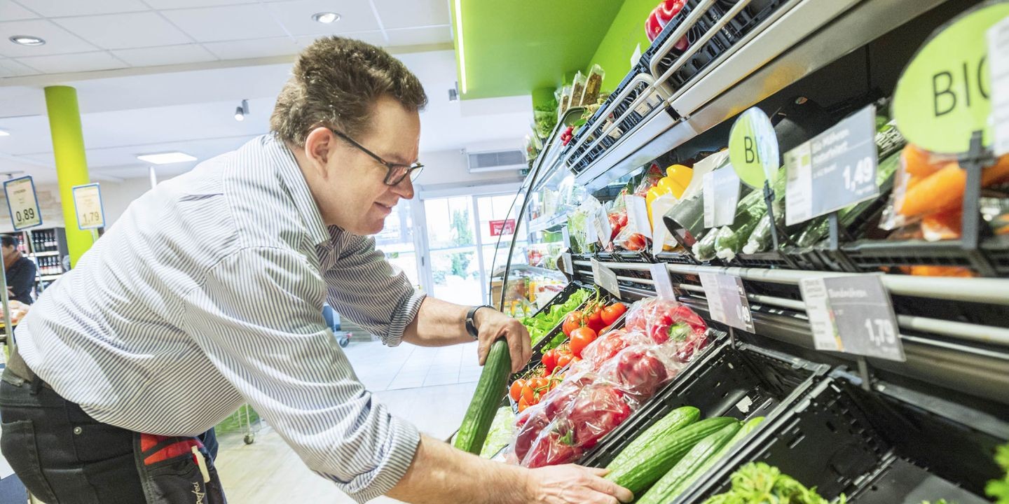 Ein Herr im Supermarkt, der die Gemüseregale auffüllt.