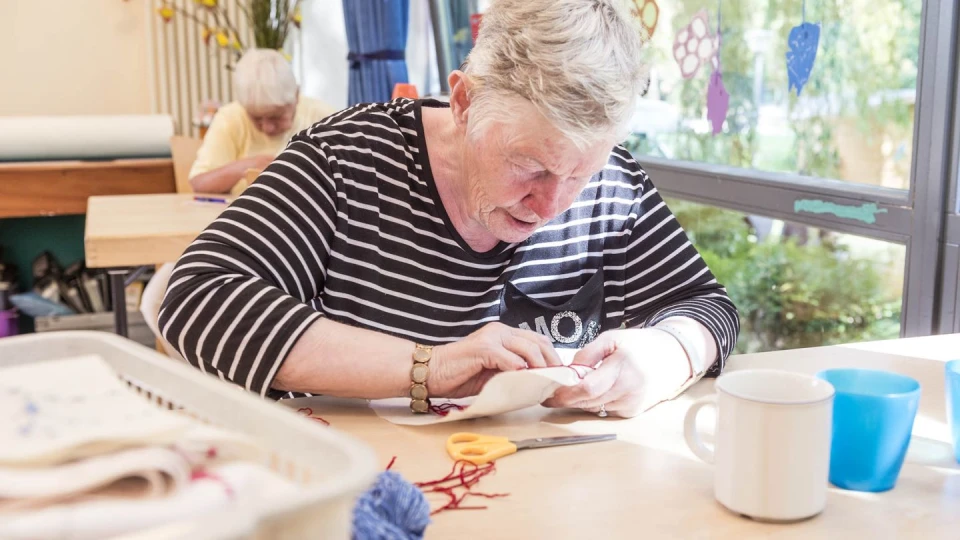 Eine Seniorin die am Tisch sitzt und bastelt.