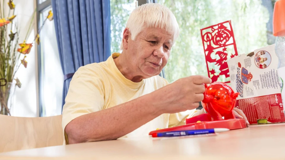 Eine Seniorin die an einem Tisch sitzt und mit einer roten Kugel spielt.