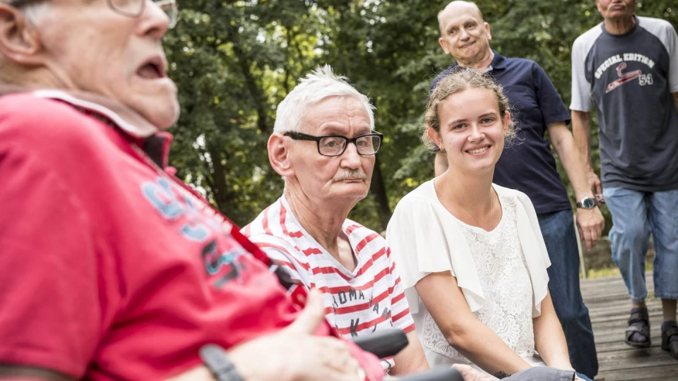 Vier Senioren und eine Pflegerin sitzen zusammen und unterhlaten sich.