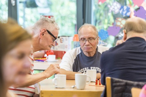 Drei Senioren sitzen zusammen an einem Tisch und spielen ein Brettsspiel.