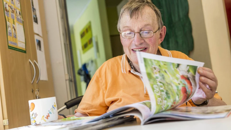 Ein Senior sitzt am Tisch und liest eine Zeitschrift.
