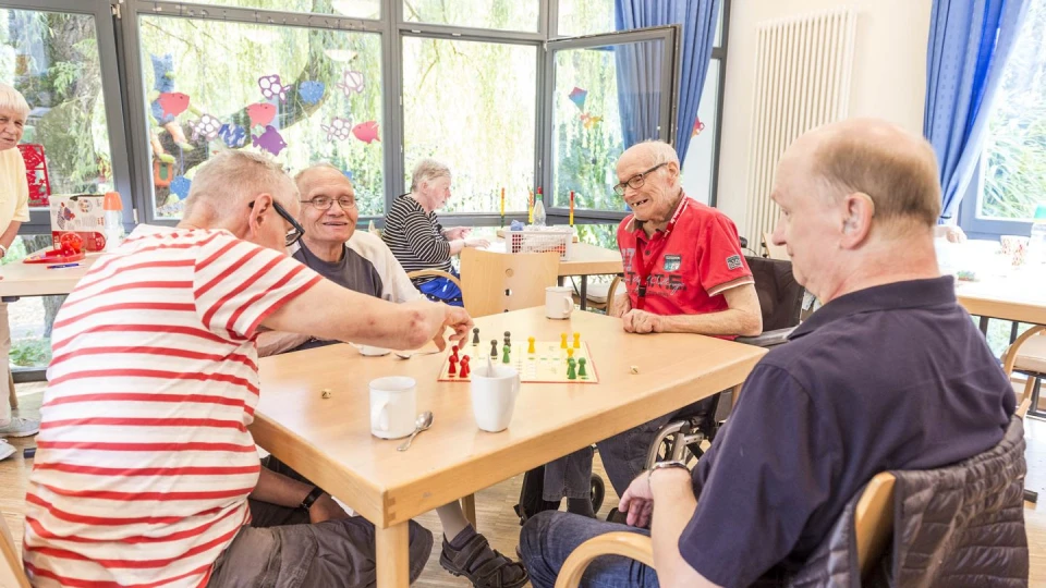 Vier Senioren sitzen zusammen am Tisch und spielen Mensch &Auml;rger Dich Nicht.