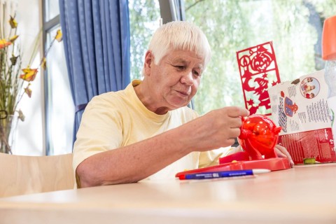 Eine Seniorin die an einem Tisch sitzt und mit einer roten Kugel spielt.