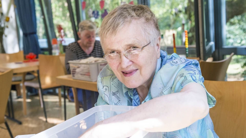 Eine Seniorin die am Tisch sitzt und in einer Kiste kramt.