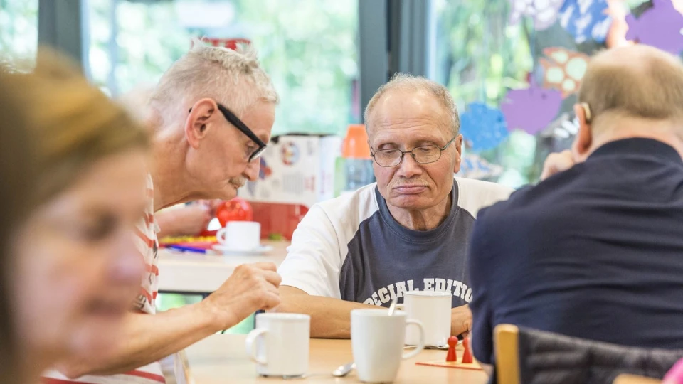 Drei Senioren sitzen zusammen an einem Tisch und spielen ein Brettsspiel.