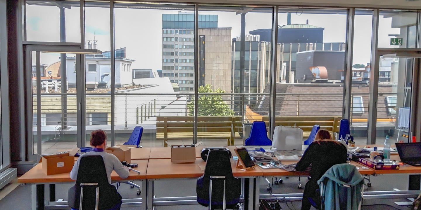 Zwei Menschen arbeiten an Computerarbeitsplätzen mit Blick auf die Dächer der Innenstadt
