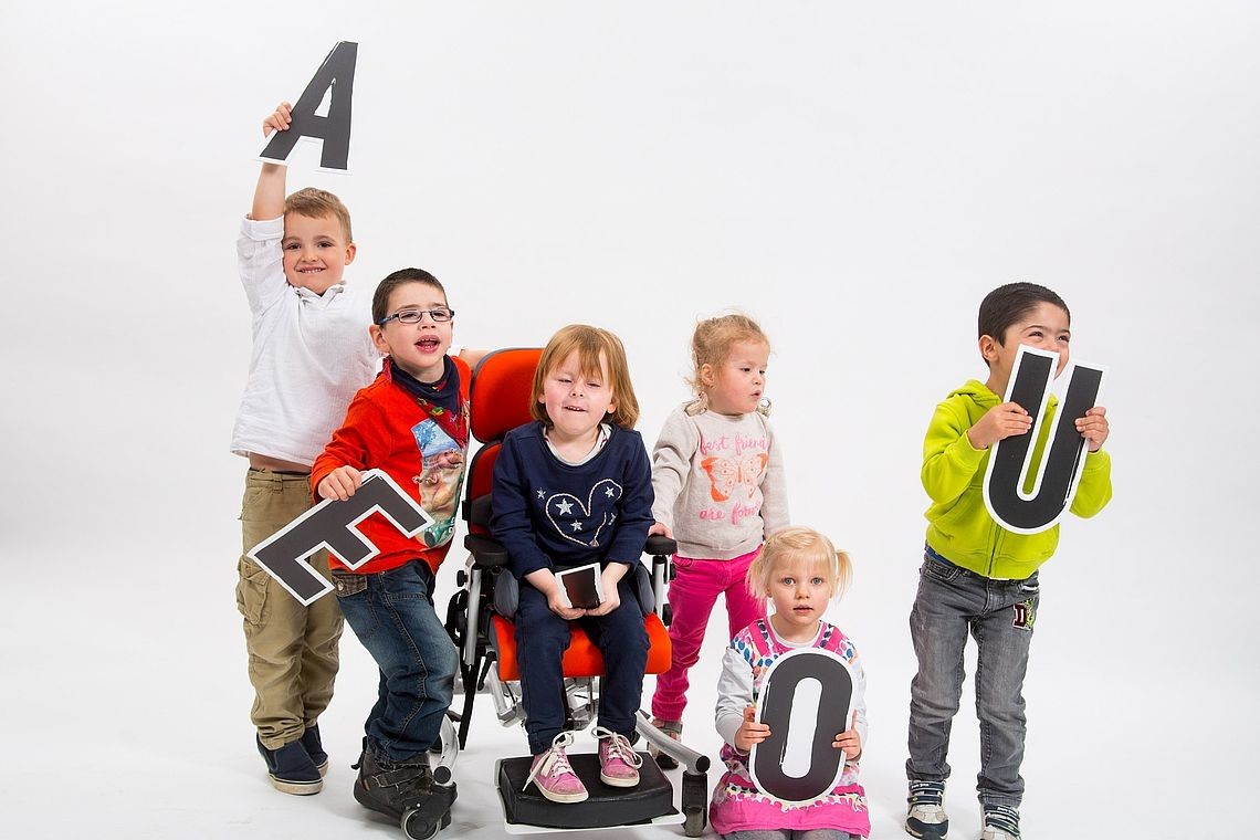 Kinder mit und ohne Beeinträchtigung halten große Pappbuchstaben hoch