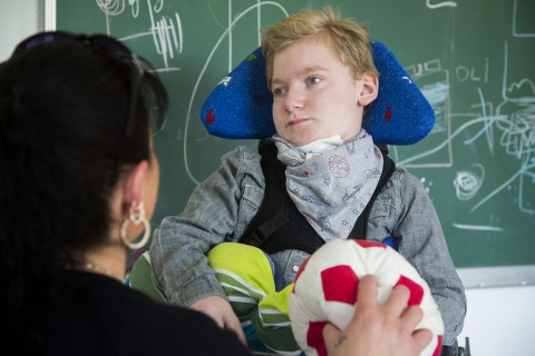 Eine Frau spricht mit einem im Rollstuhl sitzenden Kind und hält dabei einen Ball in der Hand