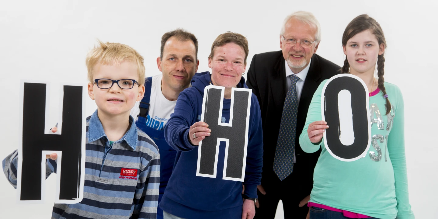5 Personen verschiedenen Alters halten die Buchstaben H, H und O hoch.