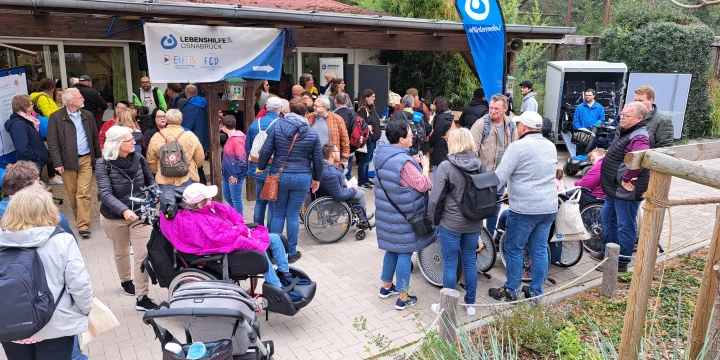 Ein Bild aus dem Zoo Osnabr&uuml;ck. An dem H&auml;uschen ist ein Banner der Lebenshilfe Osnabr&uuml;ck. Viele G&auml;ste, die der Einladung gefolgt sind, sind zu sehen.