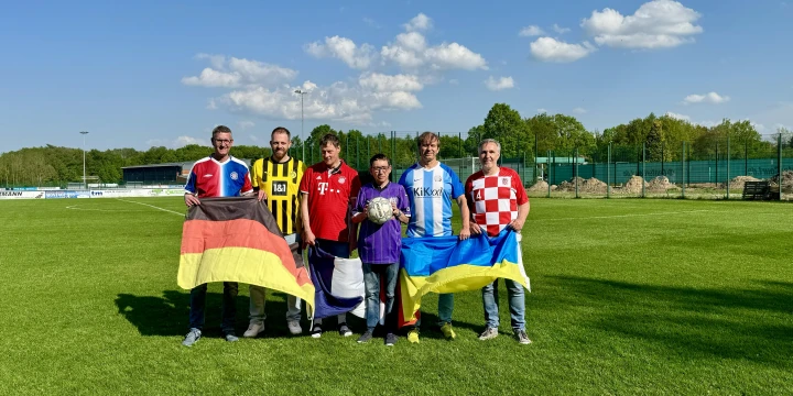Sechs M&auml;nner in Fu&szlig;balltrikots mit drei verschiedene Flaggen und einen Fu&szlig;ball halten.