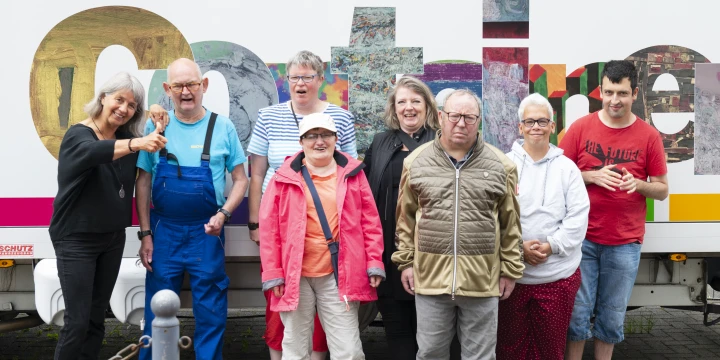 Acht Menschen stehen vor dem Auto des Kunstcontainers.