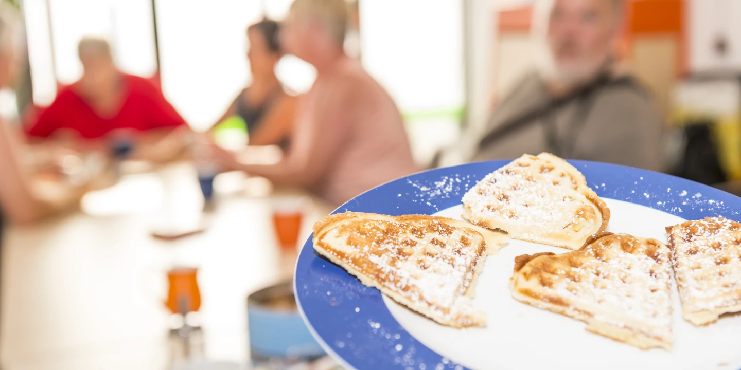 Mehrere Menschen an eine Tisch und ein Teller mit Waffeln im Vordergrund.
