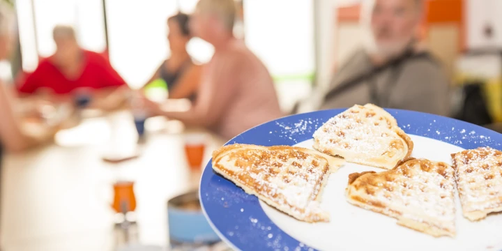Mehrere Menschen an eine Tisch und ein Teller mit Waffeln im Vordergrund.