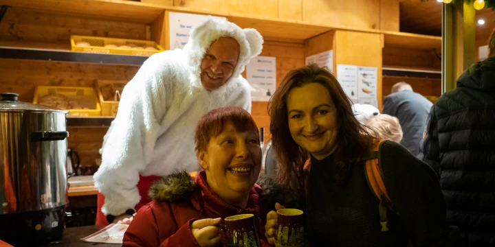 Zwei Frauen trinken eine Gl&uuml;hwein an einem Weihnachtsmarkt-B&uuml;dchen.