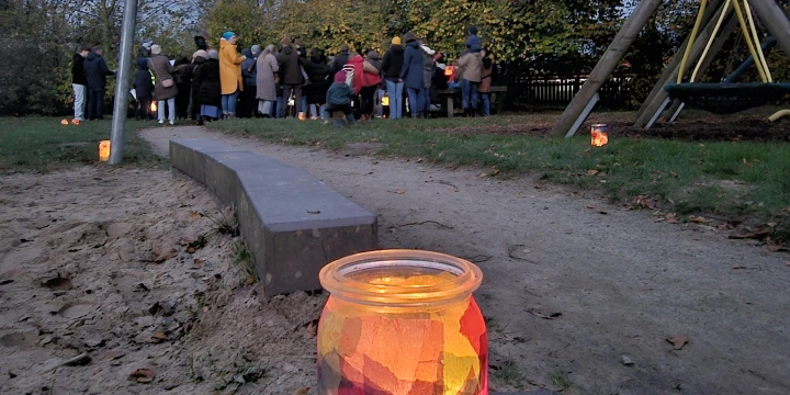 Eine Gruppe von Menschen auf einem Spielplatz und ein Buntes Teelicht im Vordergrund.