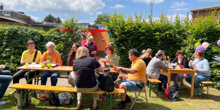 Mehrere Menschen, die auf B&auml;nken sitzen, beim Nachbarschaftsfest am Rosenplatz.