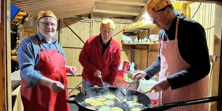 Drei M&auml;nner backen Reibekuchen in einer Pfanne.