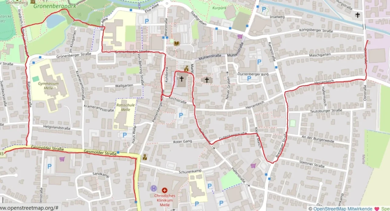 Stadtkarte mit Stra&szlig;en und Geb&auml;uden des Zentrums von Melle, Niedersachsen. Eine geschlossene, rote Linie markiert einen Rundweg, der durch mehrere Stra&szlig;en verl&auml;uft, darunter Gr&ouml;nenbergstra&szlig;e, M&uuml;hlenstra&szlig;e und Plettenberger Stra&szlig;e. Symbole f&uuml;r Parkpl&auml;tze, Kirchen und Kliniken erkennbar. Gr&uuml;nfl&auml;chen im oberen rechten und linken Bereich.