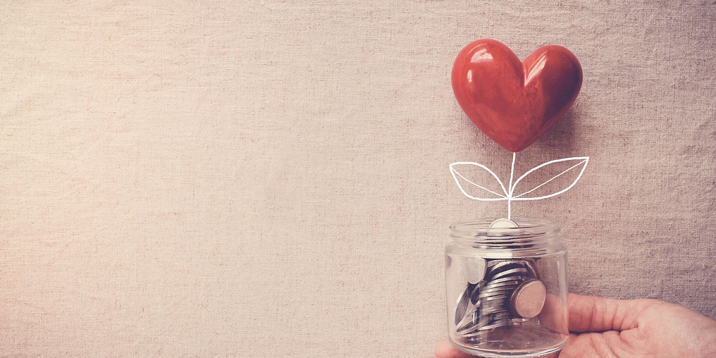 Glasbecher voller Münzen mit einem roten Herz.