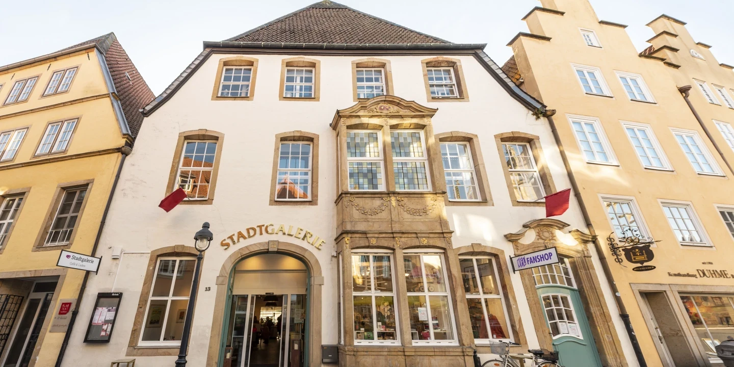 Fassade eines historischen Geb&auml;udes mit hellgelber und wei&szlig;er Au&szlig;enfassade. &Uuml;ber dem Eingang steht "STADTGALERIE" in goldfarbenen Buchstaben. Mehrere Fenster sind symmetrisch angeordnet, teilweise mit verzierten Rahmen. Rechts steht ein Fahrrad an einer Hauswand, links ein Stra&szlig;enlaterne und eine Bank. Pflastersteinstra&szlig;e im Vordergrund.