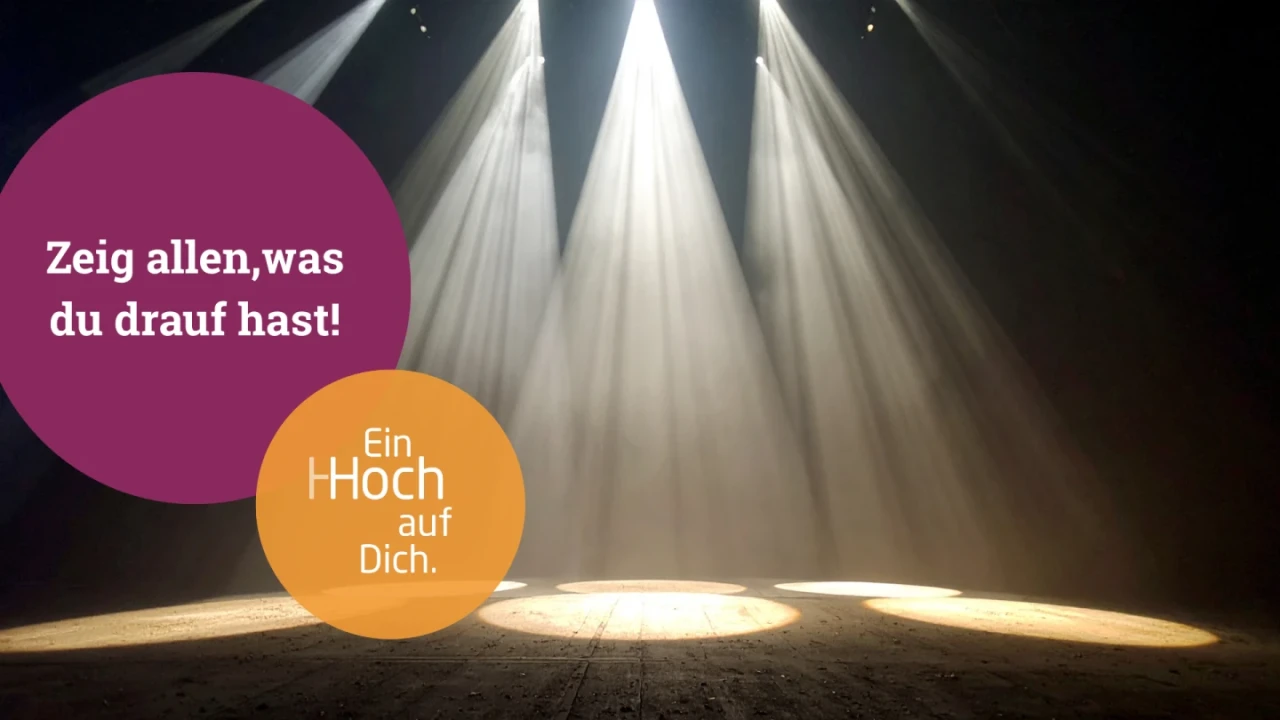 B&uuml;hnenboden in dunklem Raum, beleuchtet von f&uuml;nf hellen, fokussierten Scheinwerferstrahlen. Im Vordergrund zwei &uuml;berlappende farbige Kreise: ein violetter mit wei&szlig;em Text &bdquo;Zeig allen, was du drauf hast!&ldquo; und ein oranger mit wei&szlig;em Text &bdquo;Ein Hoch auf Dich.&ldquo;