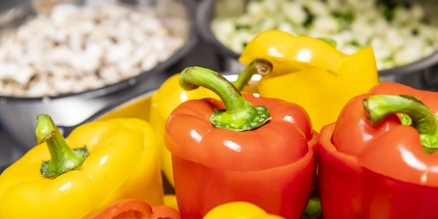 Gelbe und rote Paprika in Nahaufnahme, arrangiert im Vordergrund. Dahinter unscharfe Schalen mit geschnittenen wei&szlig;en Champignons und gew&uuml;rfelten gr&uuml;nen Zucchini.
