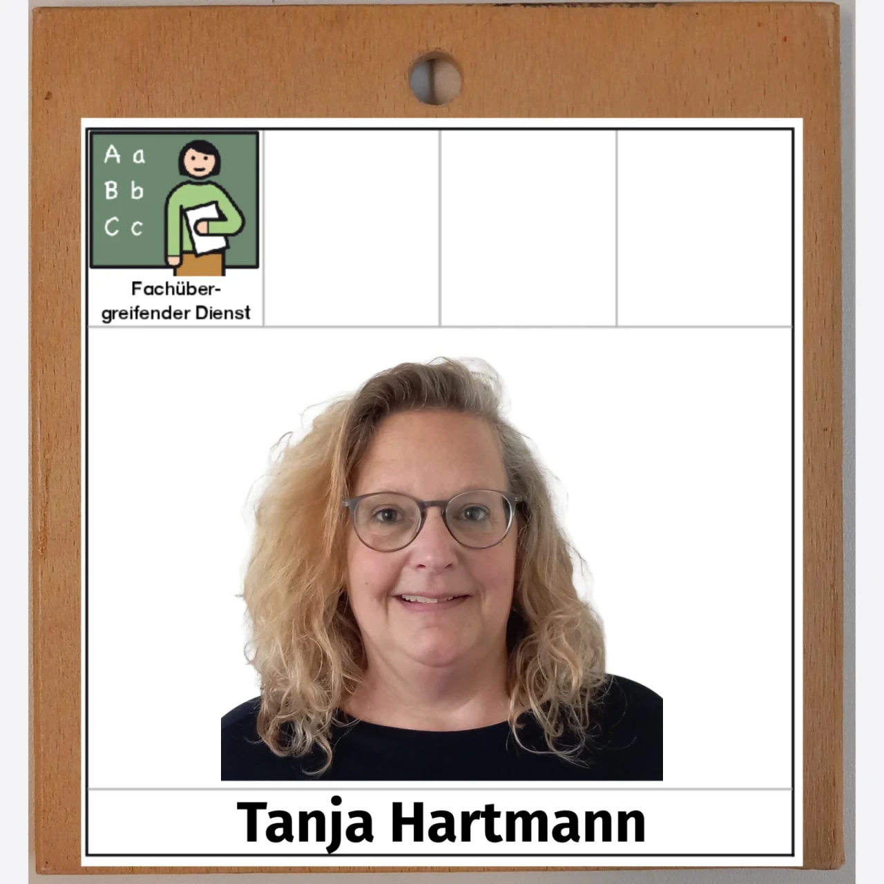 Portr&auml;tfoto einer Frau mit schulterlangem, lockigem, blondem Haar und Brille, vor einem wei&szlig;en Hintergrund. Oben links das Logo mit einem gezeichneten Symbol einer Person, Buchstaben "A", "B", "C" und der Beschriftung "Fach&uuml;bergreifender Dienst". Darunter der Name "Tanja Hartmann" in schwarzem Text auf wei&szlig;er Fl&auml;che. Holzrahmen im Hintergrund.