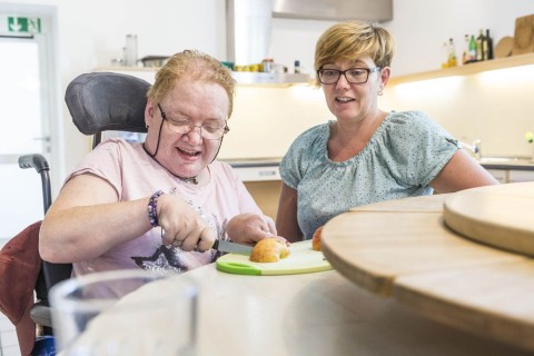 Eien Frau im Rollstuhl und eine Beteuerin schneiden einen Apfel