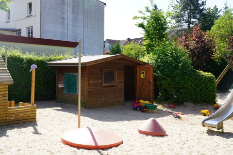 Außenbereich mit Holzhütte, Rutsche, Sandkasten und verschiedenen Spielgeräten